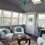 At home photography office in sunroom with separate entrance, white chairs, aqua chandelier, grey walls,